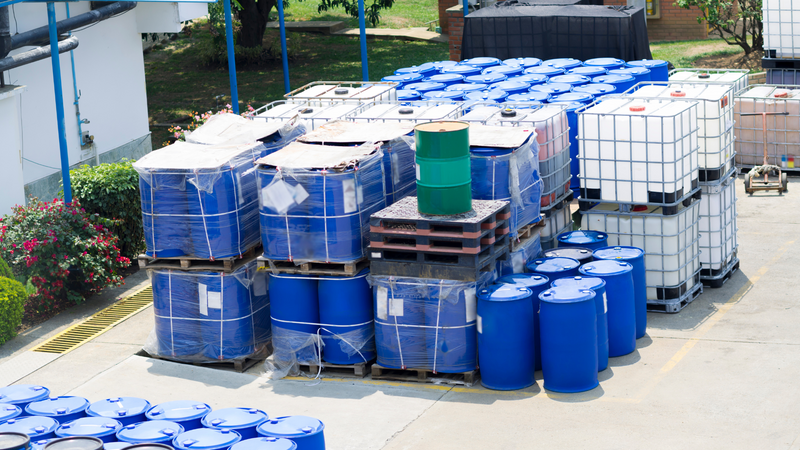 Plastic drums and IBC containers stacked in a yard outside.