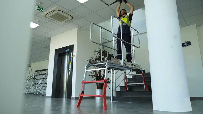 Person on a ladder inside a building with white walls and a gray floor.