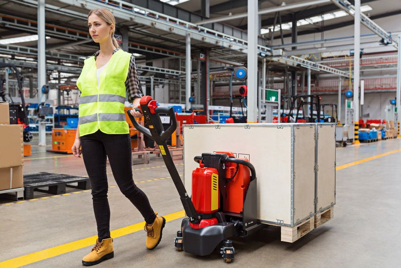Person in a warehouse using a pallet jack to move a large box.